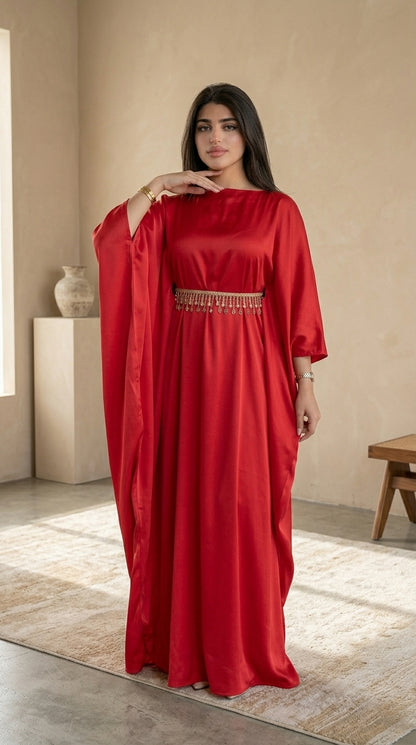 Woman wearing a red dress with a beaded waistband in a room with a beige wall and wooden floor.