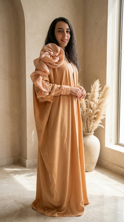 Woman wearing a long, light brown dress with a matching headscarf in a softly lit room.