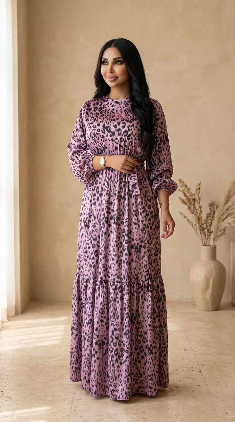 Woman wearing a long purple dress with a leopard print pattern in a room with a beige wall and vase.