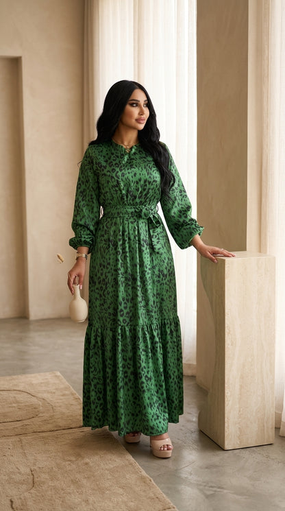 Woman in a green patterned dress standing in a room with neutral decor.