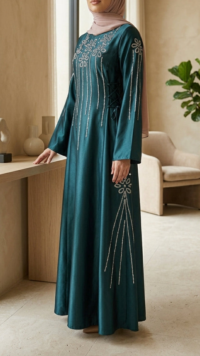 Woman in a teal dress with intricate white embroidery standing in a modern room.