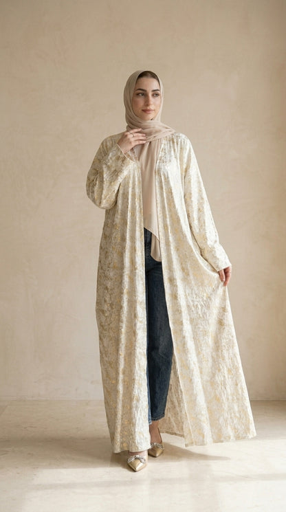 Woman wearing a long, light-colored dress with a matching hijab against a neutral background