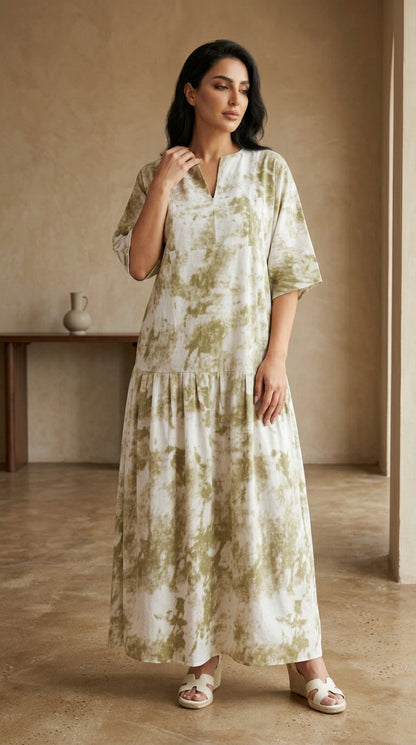 Woman wearing a long, light-colored dress with a subtle pattern in a warm-toned room.