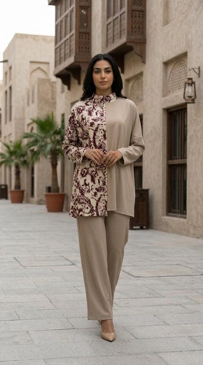 Woman in a floral top and beige pants standing in front of an architectural building.