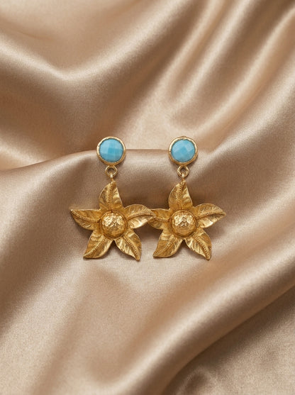 Gold earrings with turquoise stones on a beige satin background