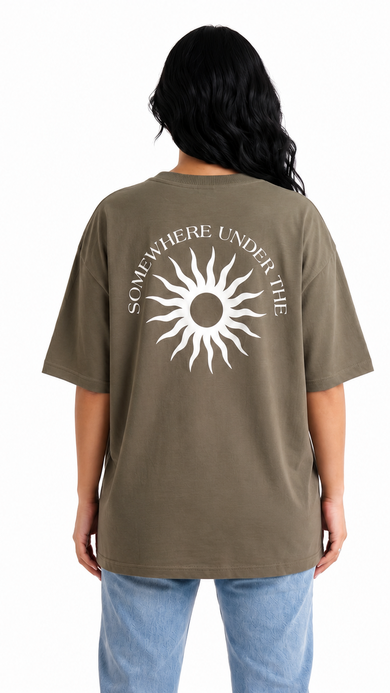 A person shown from the back wearing an oversized olive brown t-shirt with a white sun graphic and the text 'SOMETHING UNDER THE' printed on the back, paired with light blue jeans against a white background.