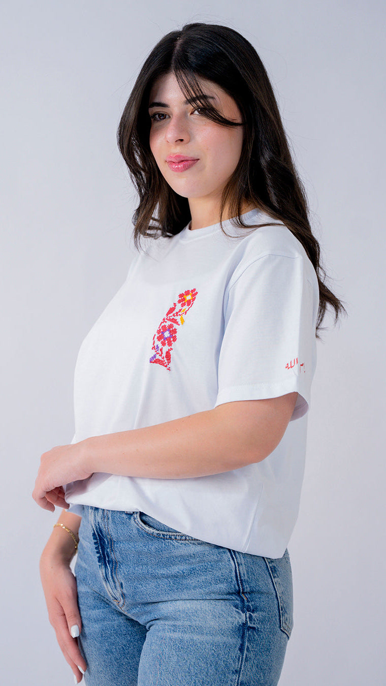 Woman wearing a white t-shirt with floral design and blue jeans on a plain background