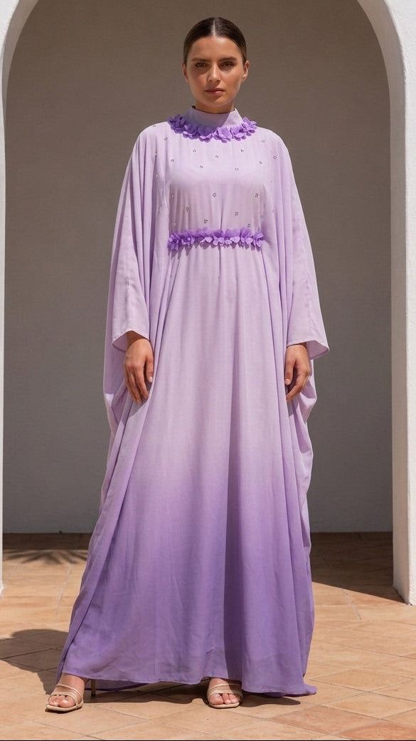 A woman wearing a lavender maxi abaya with a purple embroidered collar and waistband, standing in front of a white archway.