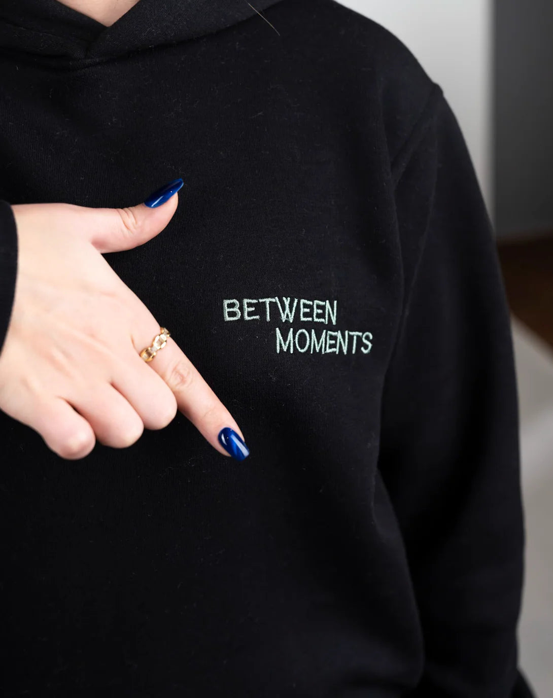 Black hoodie with 'BETWEEN MOMENTS' text, held by a person.