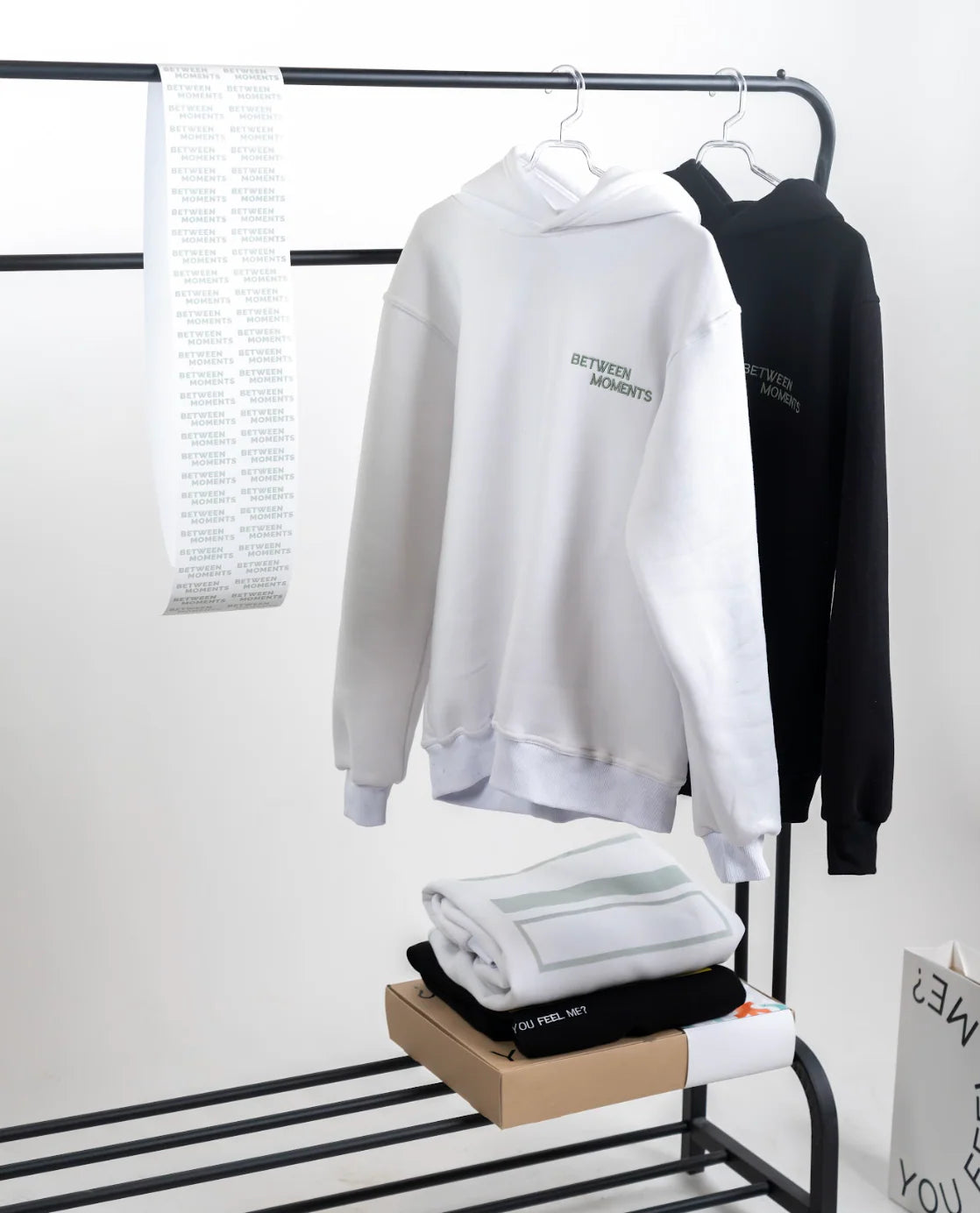 White and black hoodies on a rack with folded clothes underneath.