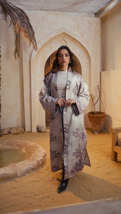Woman in a long, patterned robe standing in a decorative interior setting.
