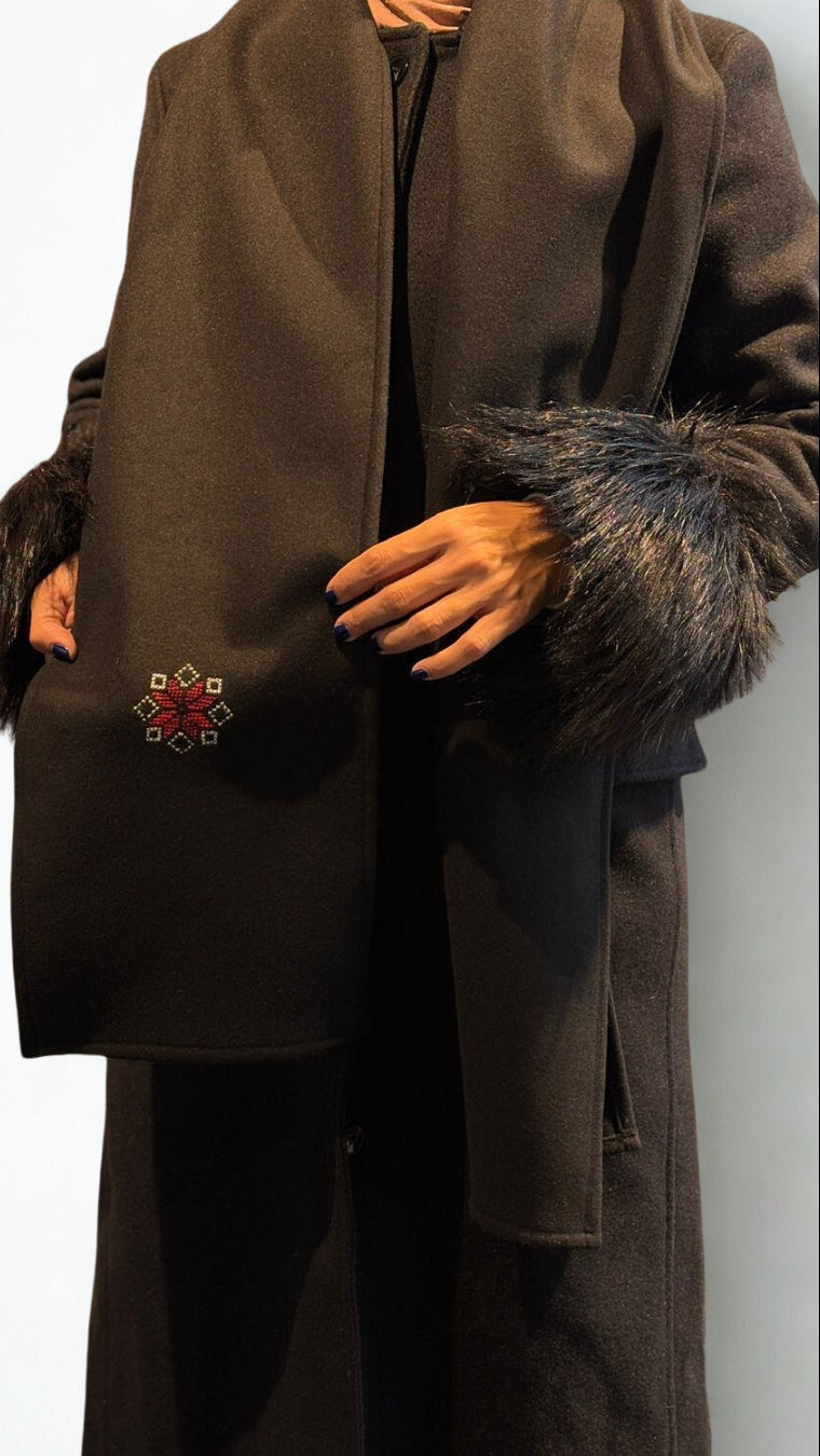 Brown coat with fur trim and a decorative emblem on a white background