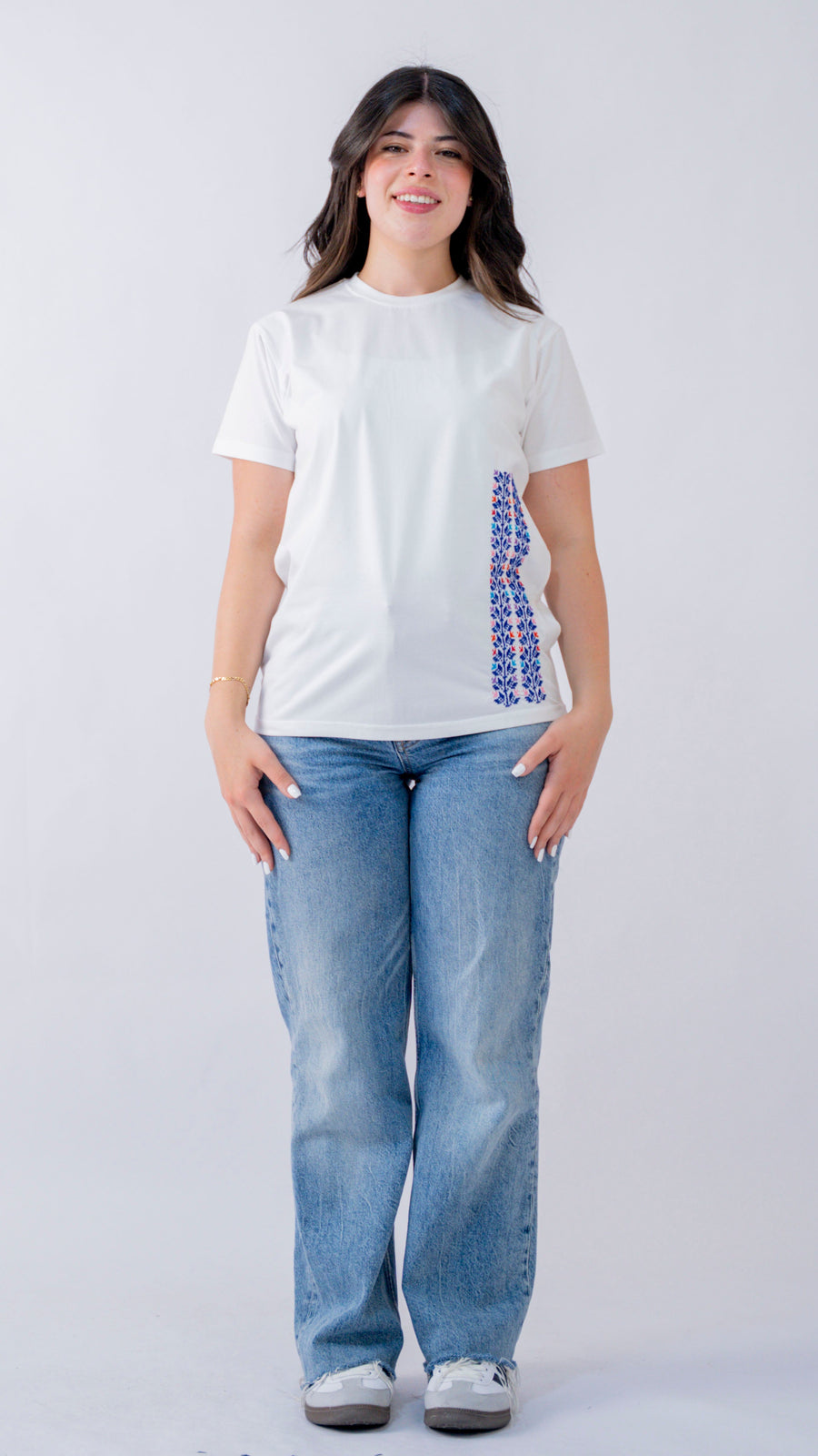 Person wearing a white t-shirt with a graphic design and blue jeans on a plain background