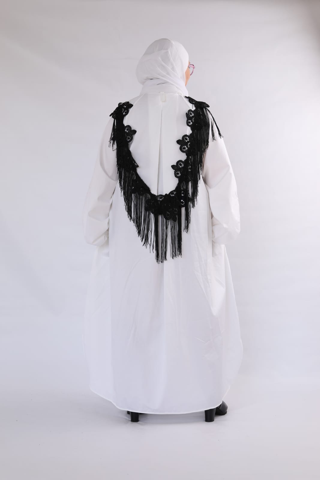 White dress with black floral embroidery and fringe on a white background