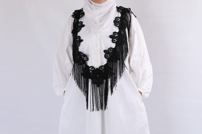 White outfit with a black fringed accessory on a plain background