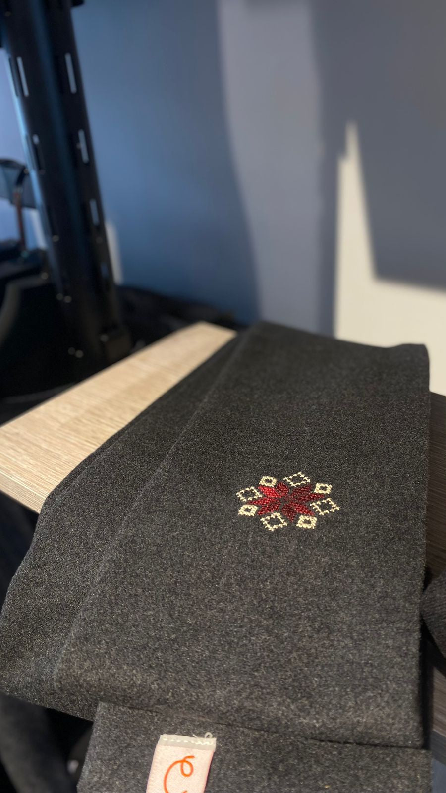 Dark gray scarf with a red and white embroidered design on a wooden surface.