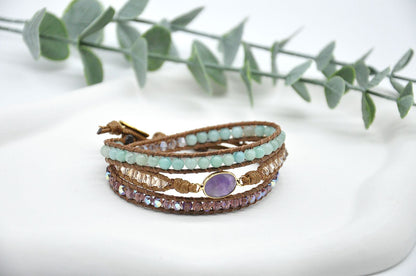 Multistrand bracelet with beads and a purple gemstone on a white surface with green leaves in the background