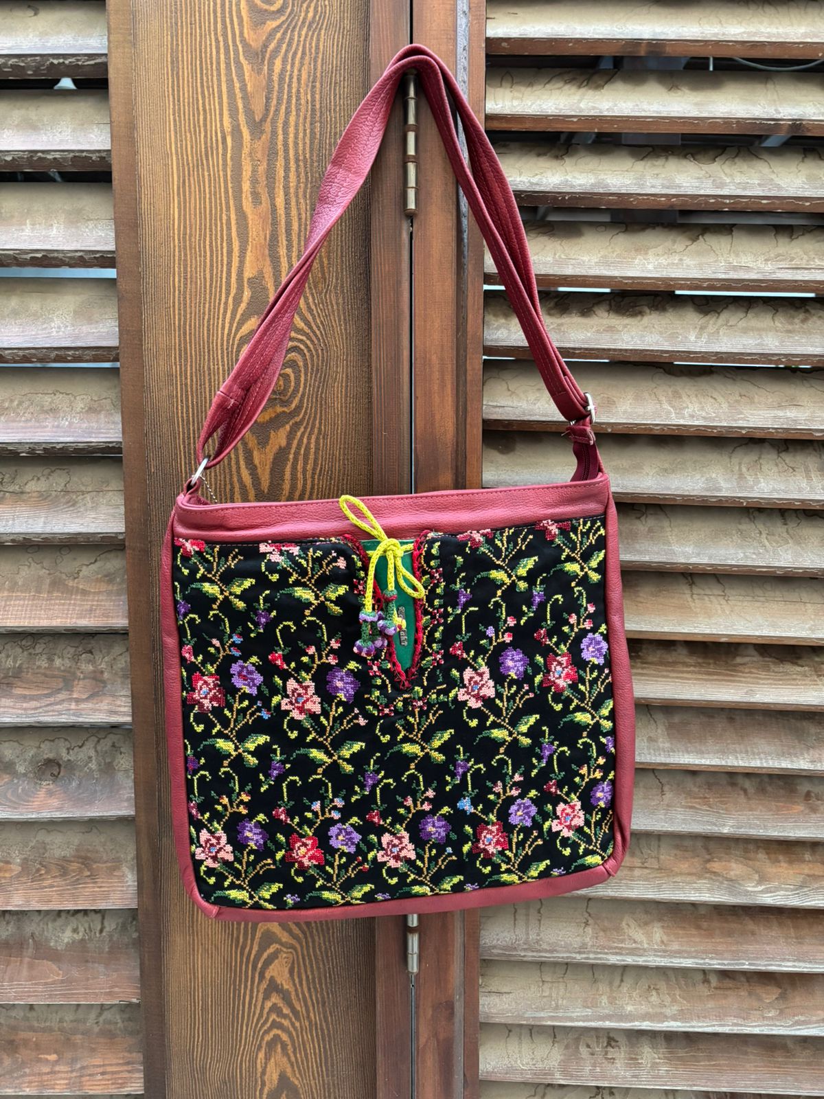 Floral-patterned bag with a red strap hanging on wooden slats