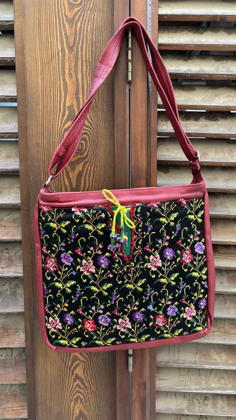 Floral-patterned bag with a red strap hanging on wooden slats