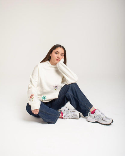 Person wearing a white sweater and blue jeans sitting on the floor against a plain background