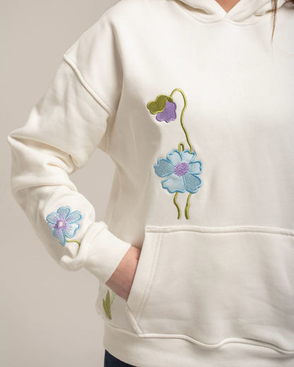 White hoodie with floral designs on the sleeves against a neutral background
