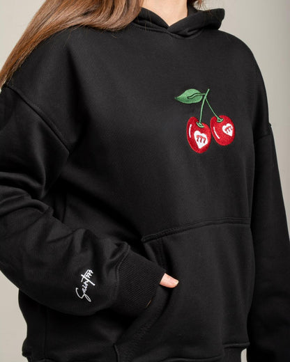 Black hoodie with cherry design on a neutral background