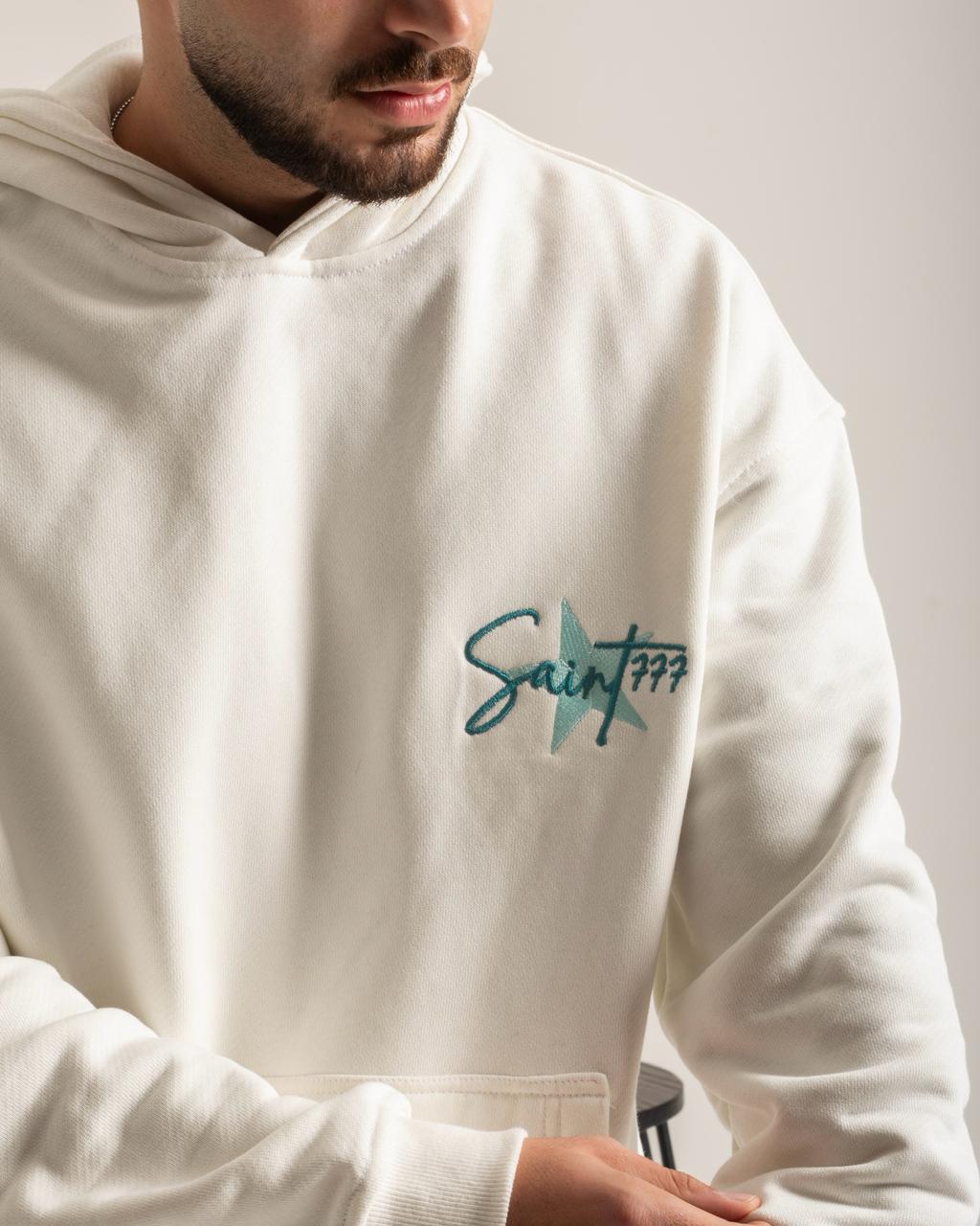 White hoodie with 'Saint 777' logo worn by a person, on a plain background