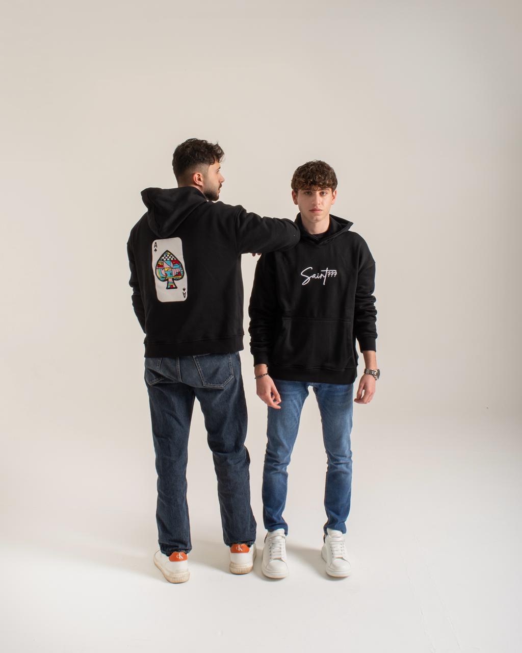 Two people wearing black hoodies with visible branding on a plain background