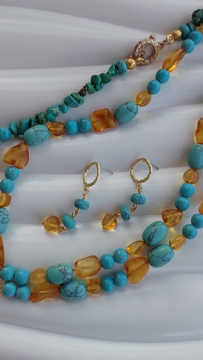 A multi-strand turquoise and amber beaded necklace set with matching drop earrings, displayed on a white wavy surface.