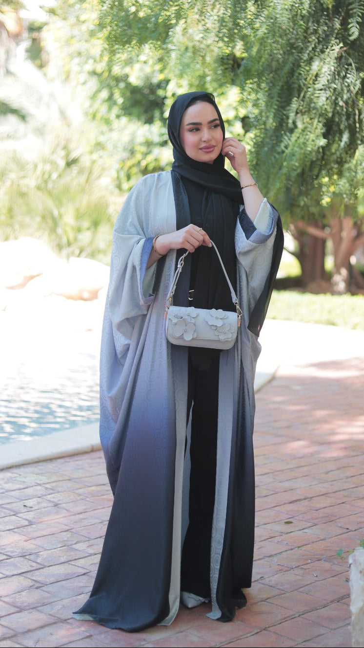 Woman in a gray and black outfit with a headscarf standing outdoors near trees and a pool.