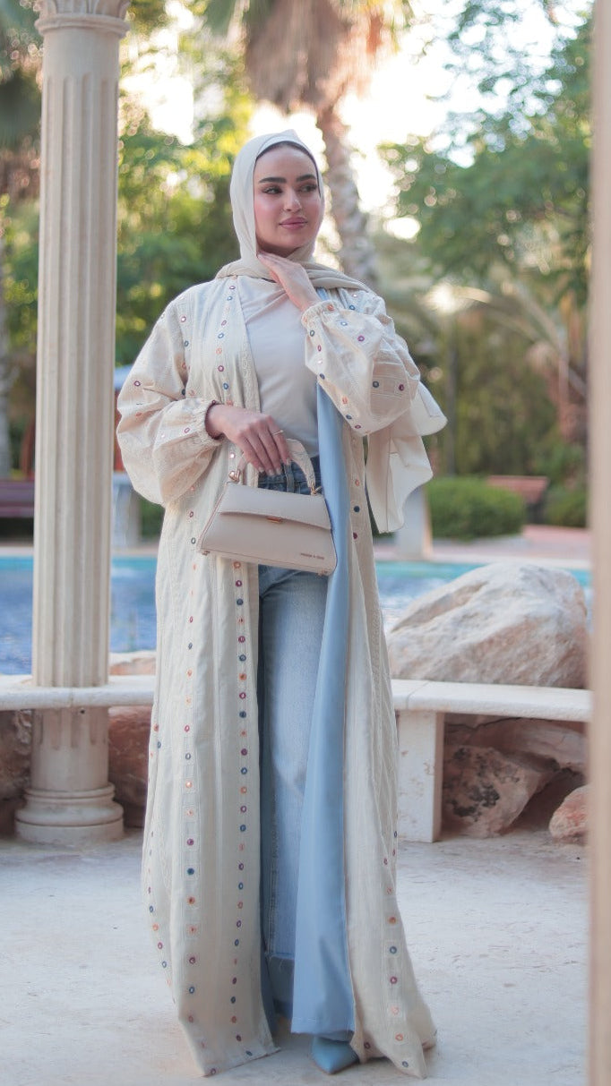 Woman in a long, light-colored dress standing in a scenic outdoor setting with columns and greenery.