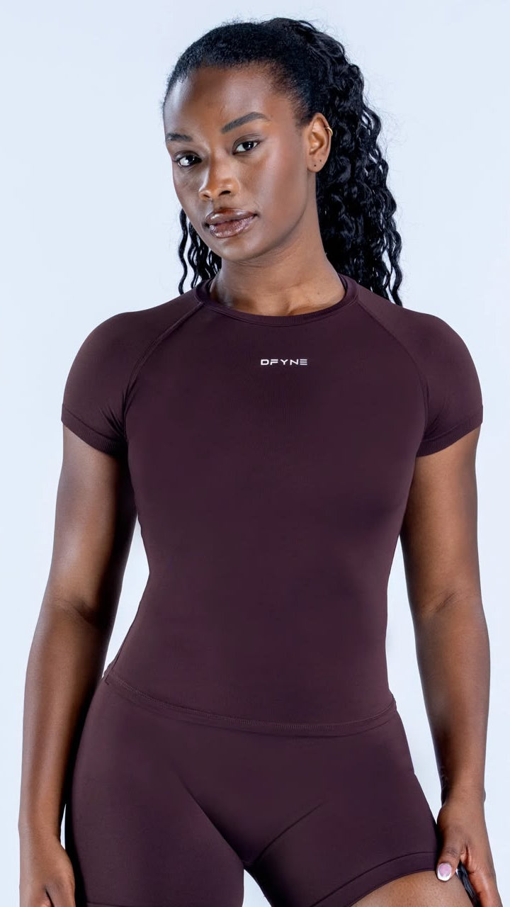 Woman wearing a maroon athletic outfit with a visible brand logo on a light gray background