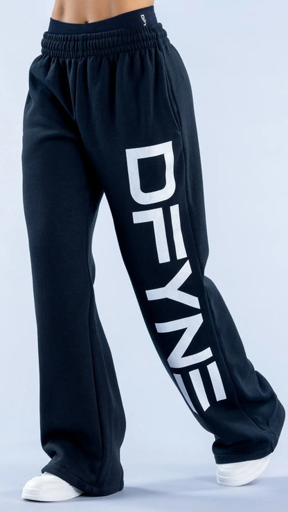 Black wide-leg sweatpants with a large white vertical 'DFYNE' logo printed on the left leg, shown on a model from the waist down against a light gray studio background.