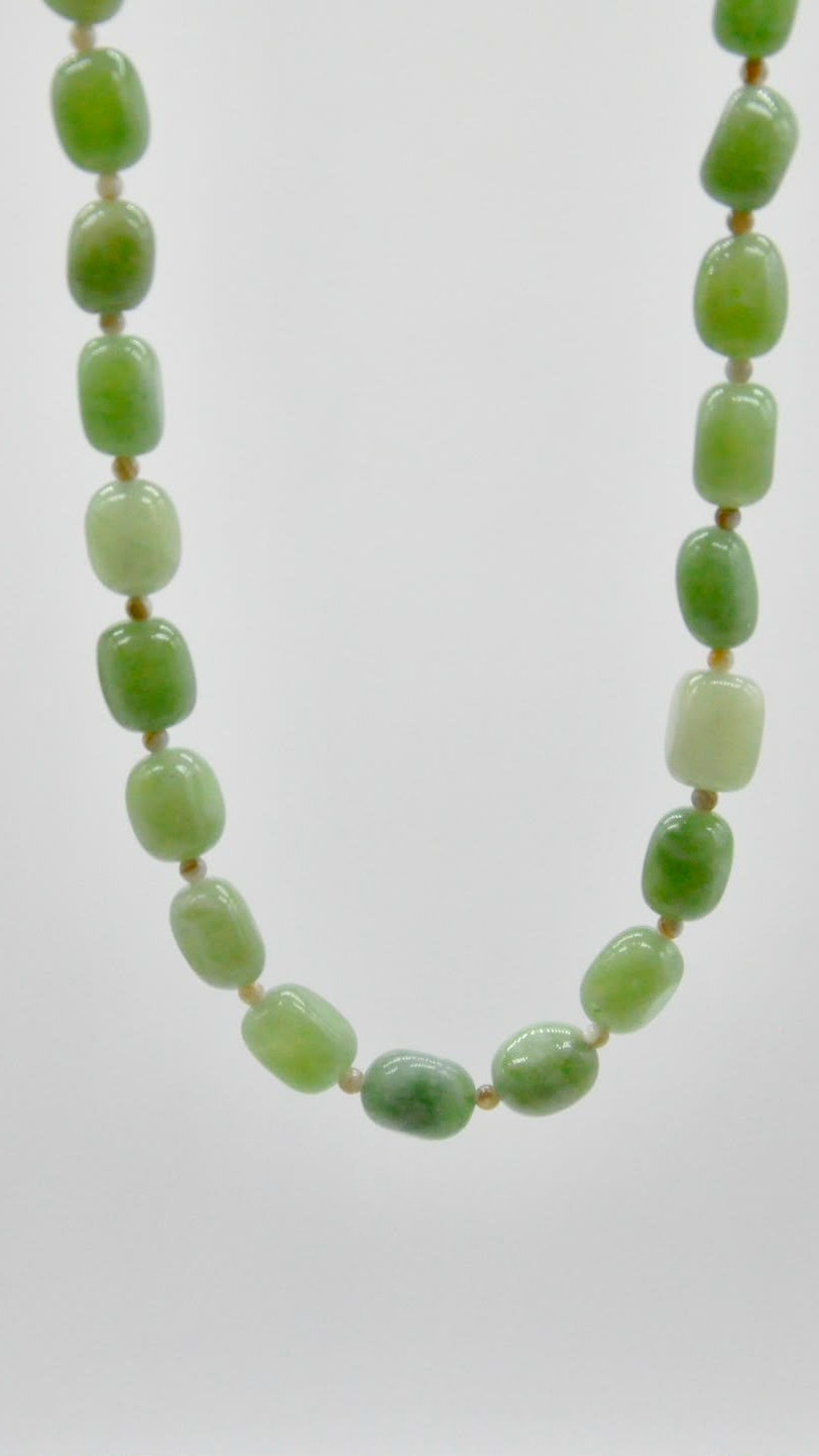 A beaded necklace made of polished green stone beads with a small gold spacer between each bead, shown against a plain light gray background.