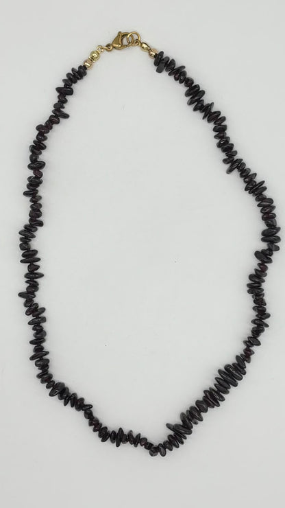 A black chip-stone necklace with a gold lobster clasp, laid flat on a light gray background.