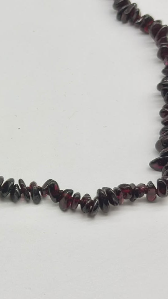 A strand of dark reddish-brown polished gemstone chips, likely garnet, arranged in a curved line on a plain white background.