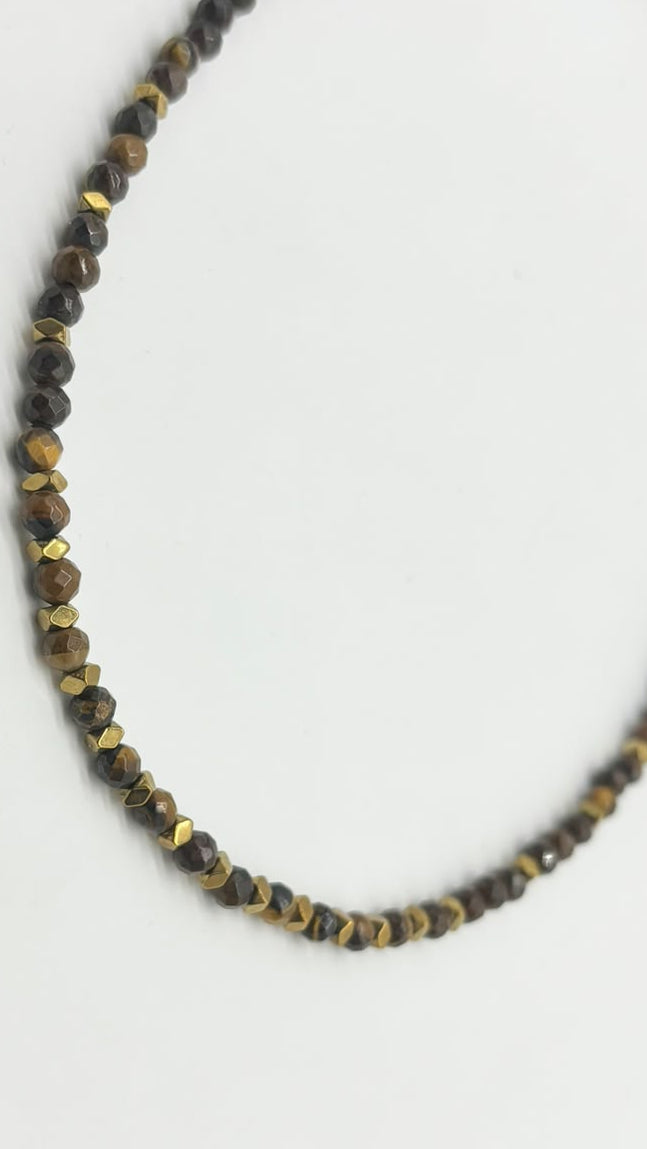 A beaded necklace made of small faceted brown and black beads with metallic gold accents, displayed on a plain white background.