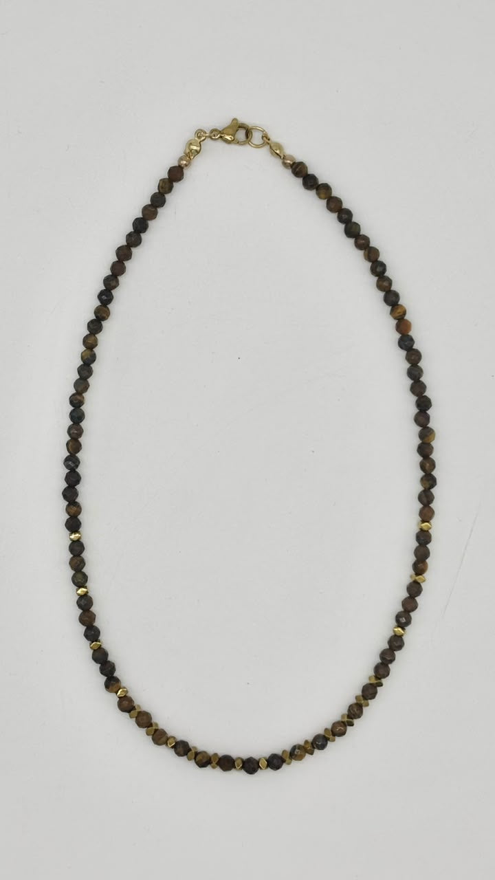 A beaded necklace made of small dark brown and black faceted beads with small gold spacer beads and a gold clasp, displayed on a light gray background.