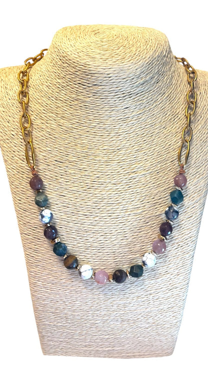 A gold-tone chain necklace with faceted multicolor beads, displayed on a beige textured mannequin bust against a white background.