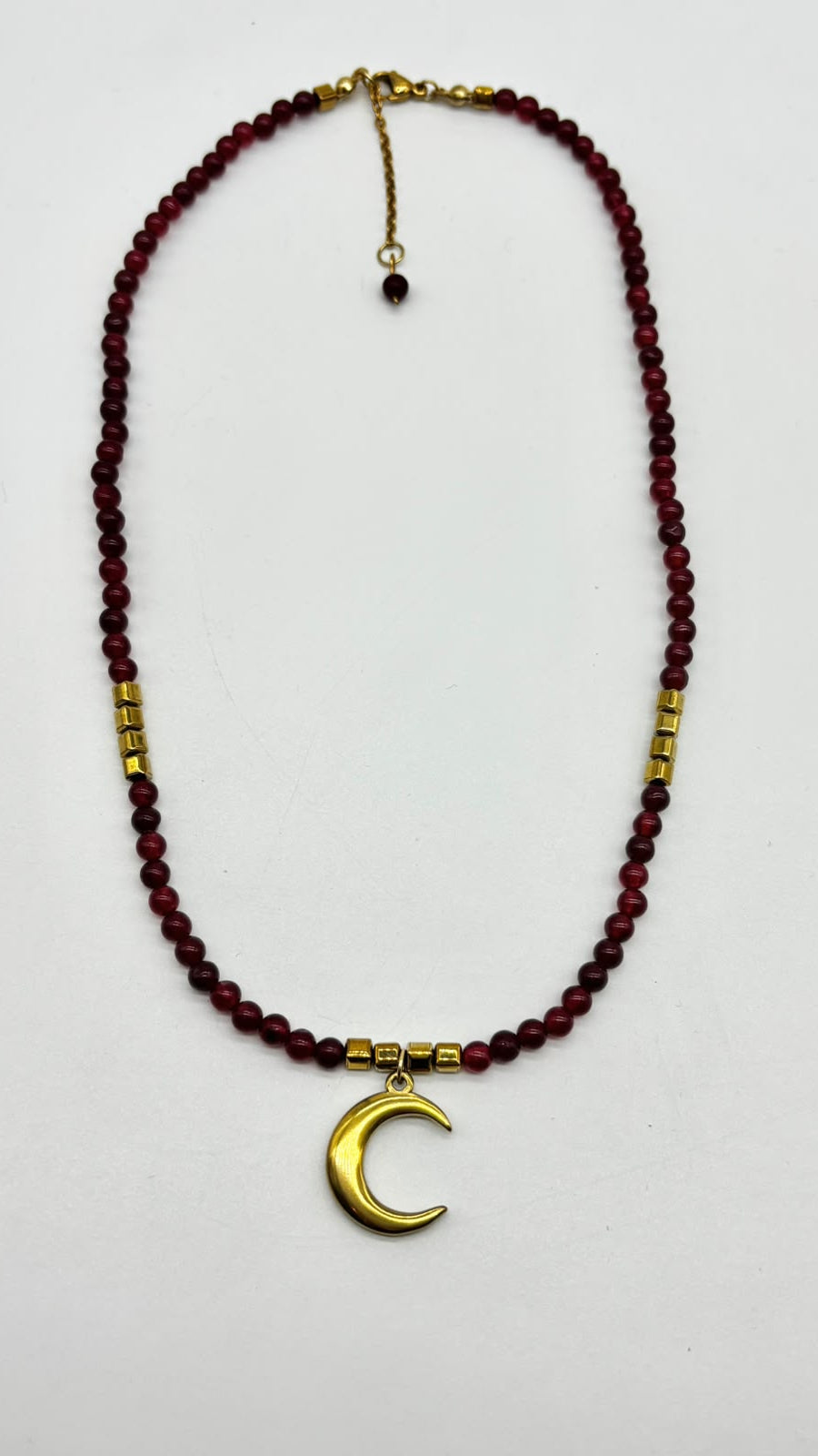 A beaded necklace featuring dark red round beads, gold spacer beads, and a gold crescent moon pendant, displayed on a plain white background.