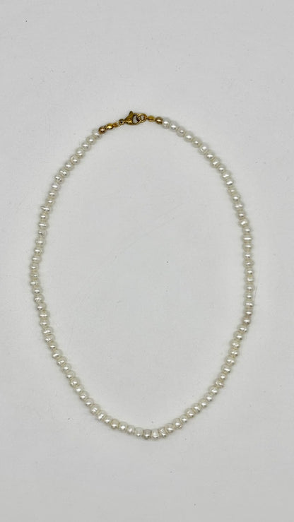 A single-strand pearl necklace with a gold clasp, laid flat on a light gray background.