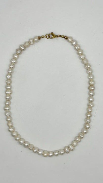 A strand of irregular white freshwater pearls with a gold clasp, laid flat on a light gray background.