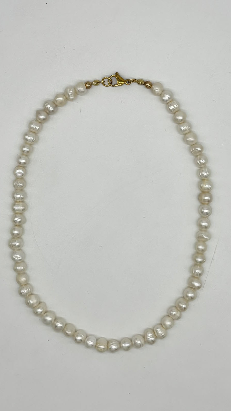 A strand of irregular white freshwater pearls with a gold clasp, laid flat on a light gray background.