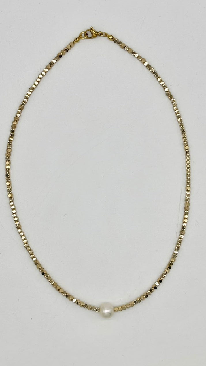 A delicate gold chain necklace with a single small white pearl bead at the center, laid flat on a light gray background.
