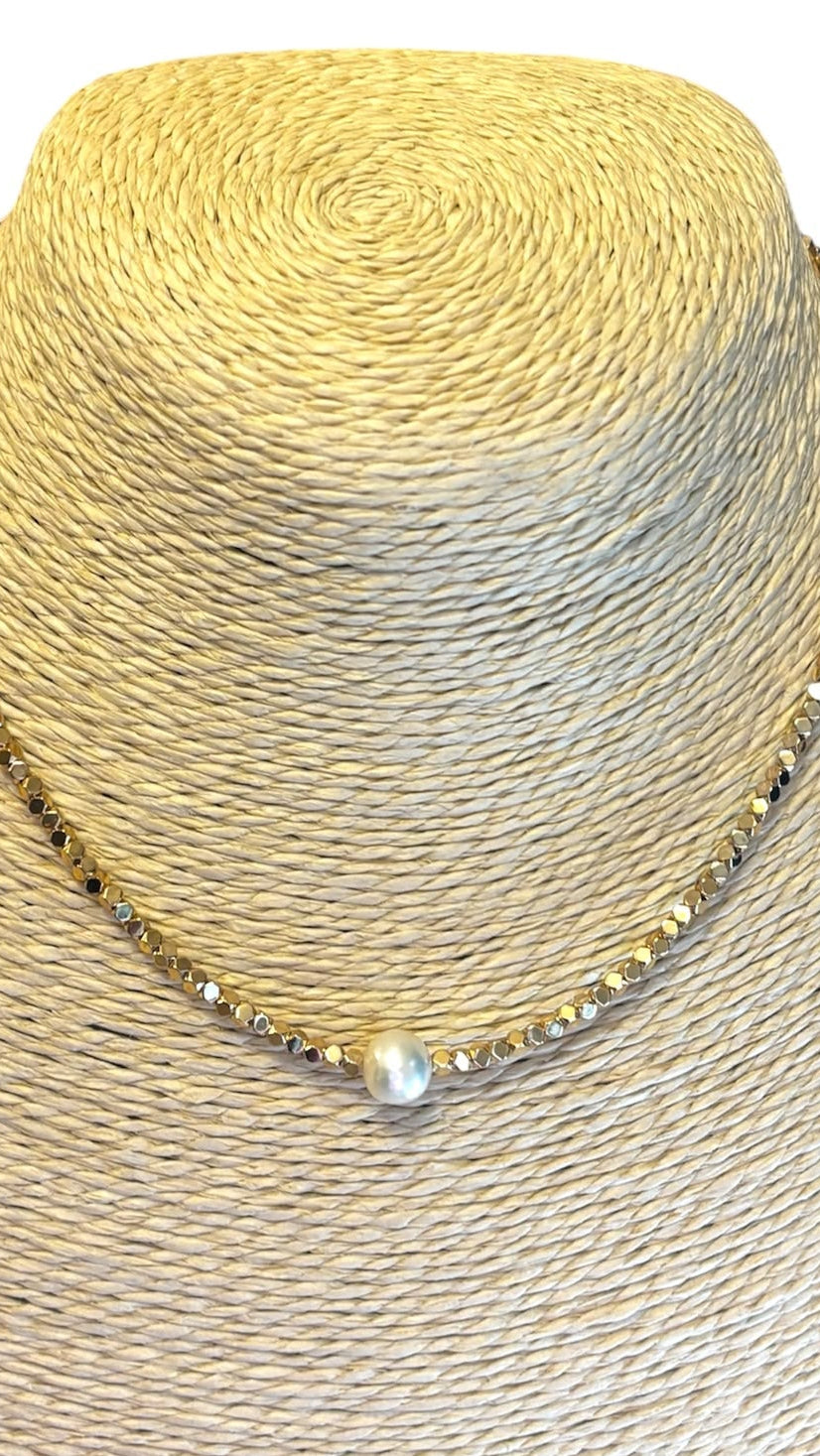 A delicate gold chain necklace with a single white pearl pendant, displayed on a beige woven mannequin bust against a white background.