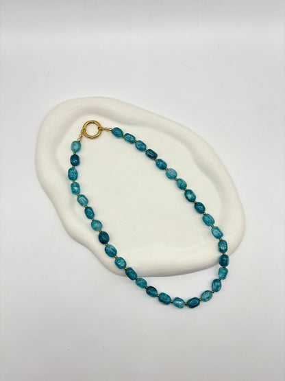 Blue beaded necklace on a white dish with a white background