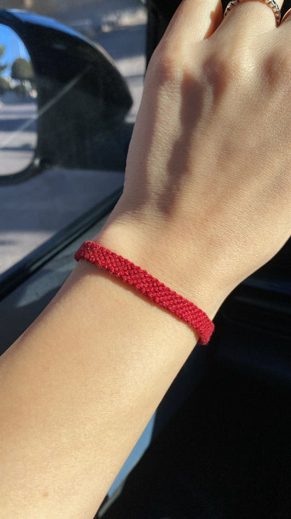 Hand wearing a red bracelet with a blurred background