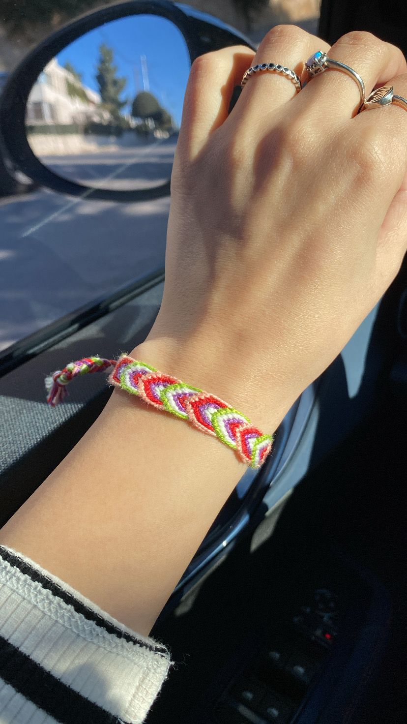 Hand wearing a colorful braided bracelet with a car interior background