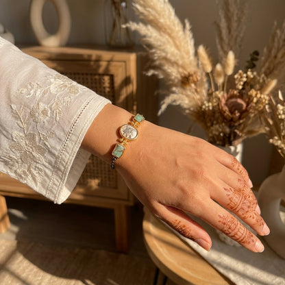 Hand wearing a gold bracelet with turquoise stones, set against a warm-toned background.