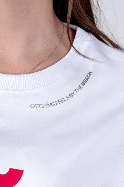 White sweatshirt with text 'Catching Feels by the Beach' worn by a person.
